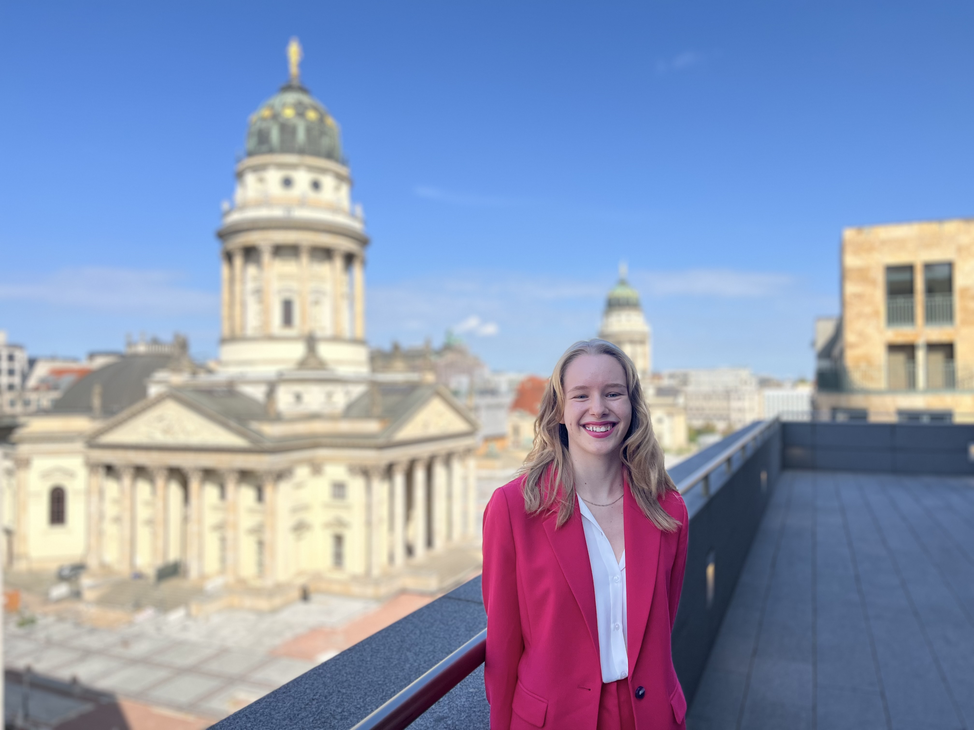 Foto showing a young woman, Leatizia Schulz, who has been a participant of the Dentons Summer Internship program Meet Dentons standing on a balcony with the Gandarmenmarkt in the background. 