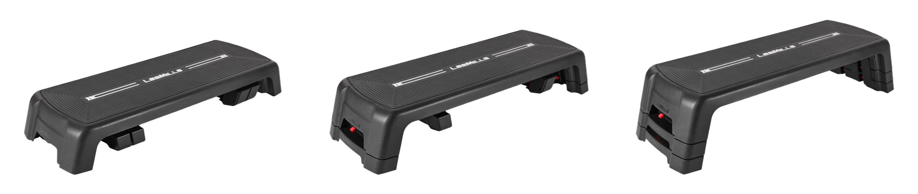 Image showing three Les Mills SMARTSTEP platforms, positioned side by side to demonstrate different height adjustments. Each step is rectangular with a textured, non-slip black surface and the white Les Mills logo printed in the centre. The sides of the steps are slightly rounded with sturdy legs at each corner. Beneath the platform, risers can be added or removed to change the height. The step on the left is set at the lowest height, with only the base platform and no risers attached. The middle step is raised slightly higher with one set of risers locked into place under the legs, creating a more elevated platform. The step on the right is shown at the highest setting with two sets of risers stacked neatly under the legs for maximum height. The red locking clips on the sides of the risers are visible, securing them in place. All three steps are black, uniform in shape, and displayed against a plain white background to highlight the adjustable height feature.