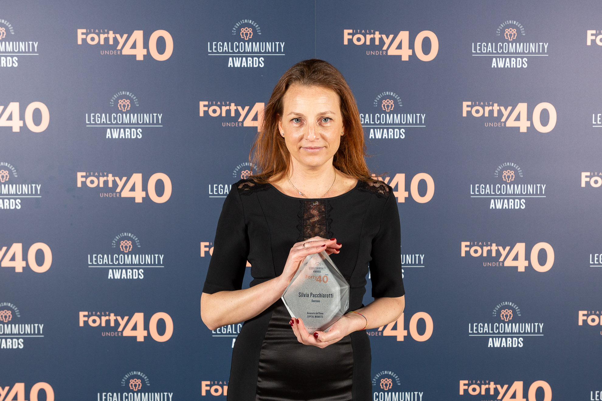 Silvia Pacchiarottii standing in front of a wall and holding an Legal Community award in her hands